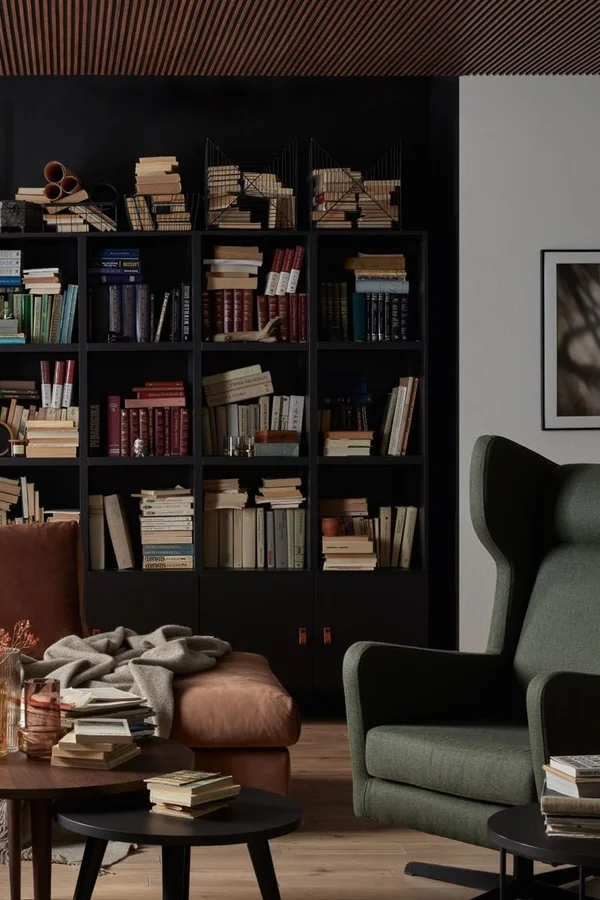 Elegancka biblioteka z czarnym regałem pełnym książek, ciemnozielonym fotelem i skórzaną sofą w ciepłym odcieniu brązu.
